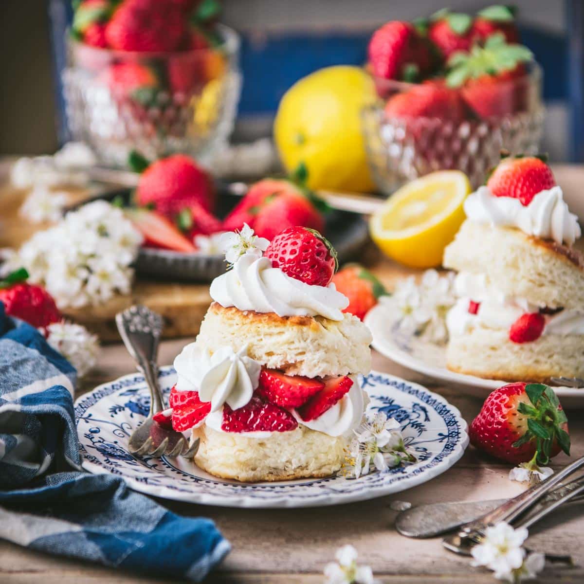 Table of strawberry shortcake with fresh berries and lemons in the background.