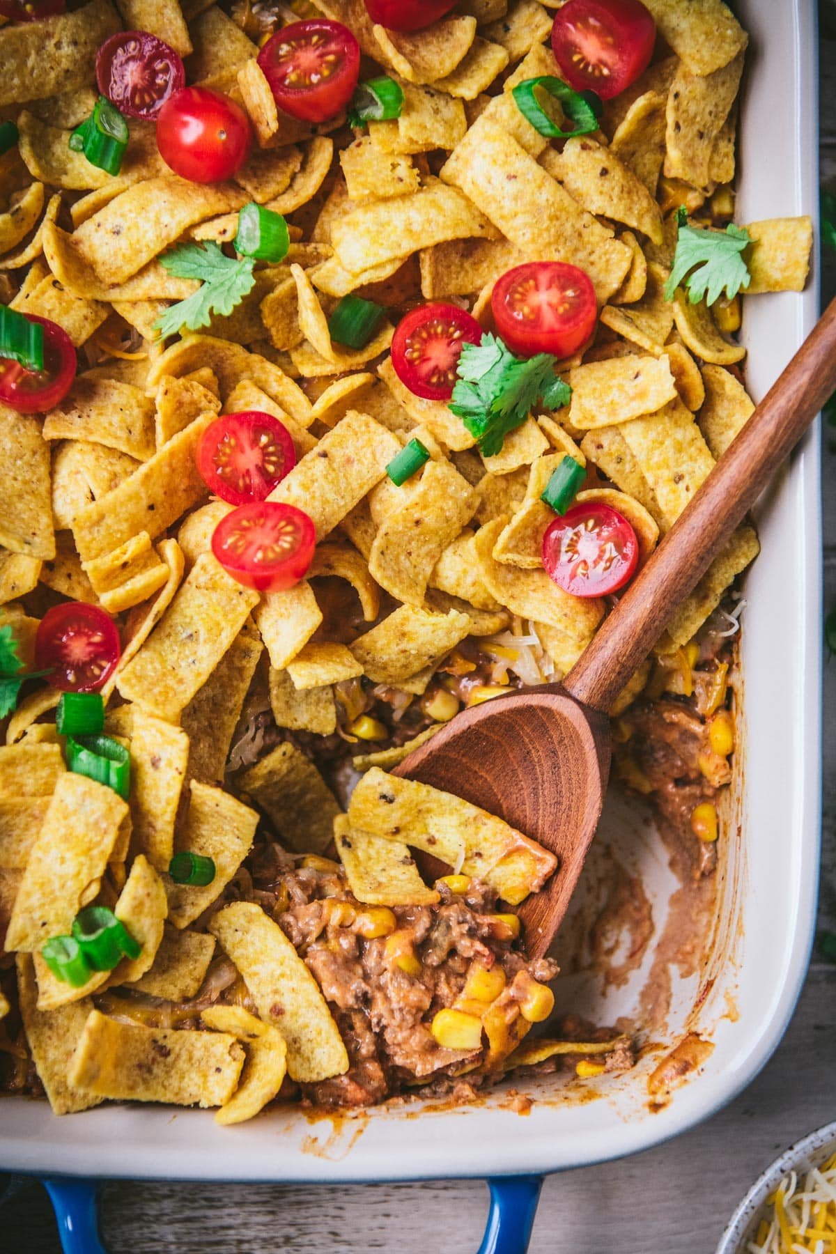 Close overhead image of a wooden spoon in walking taco bake with fritos.