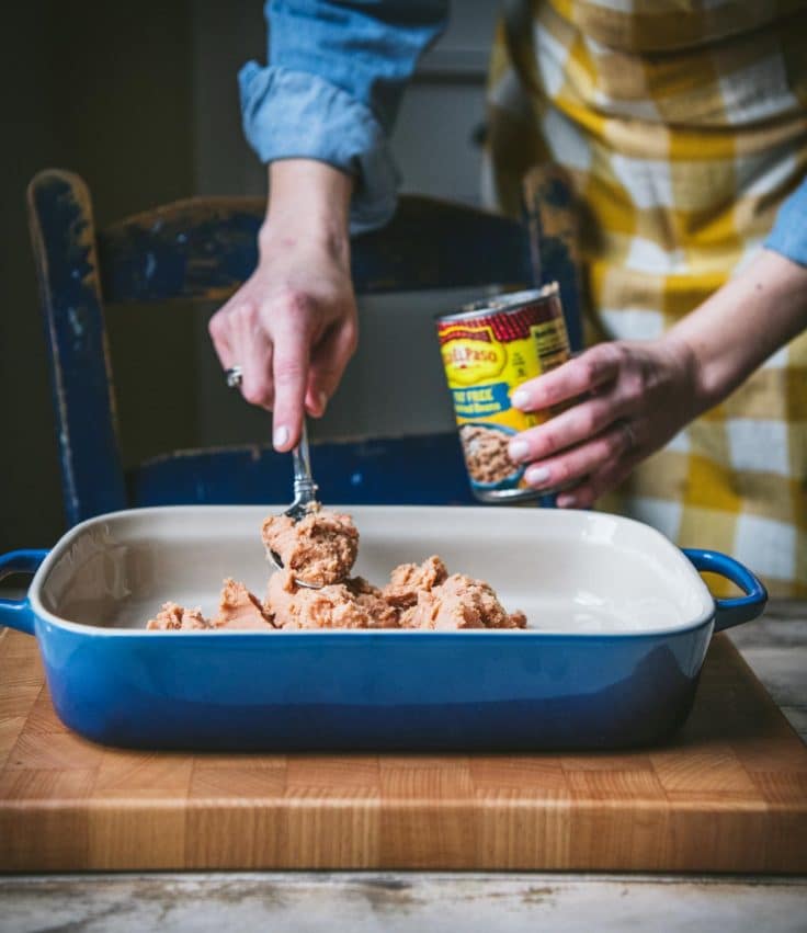 Spreading refried beans in a blue casserole dish