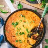 Easy tamale pie on a wooden dinner table with cilantro and lime wedges for garnish.