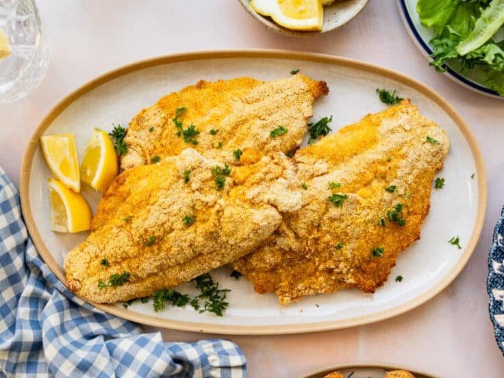 Oven baked catfish served on a white oval platter with parsley garnish and fresh lemon.