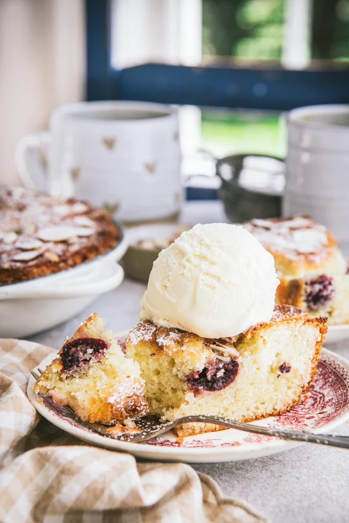 Slice of cherry cake on a plate with ice cream.