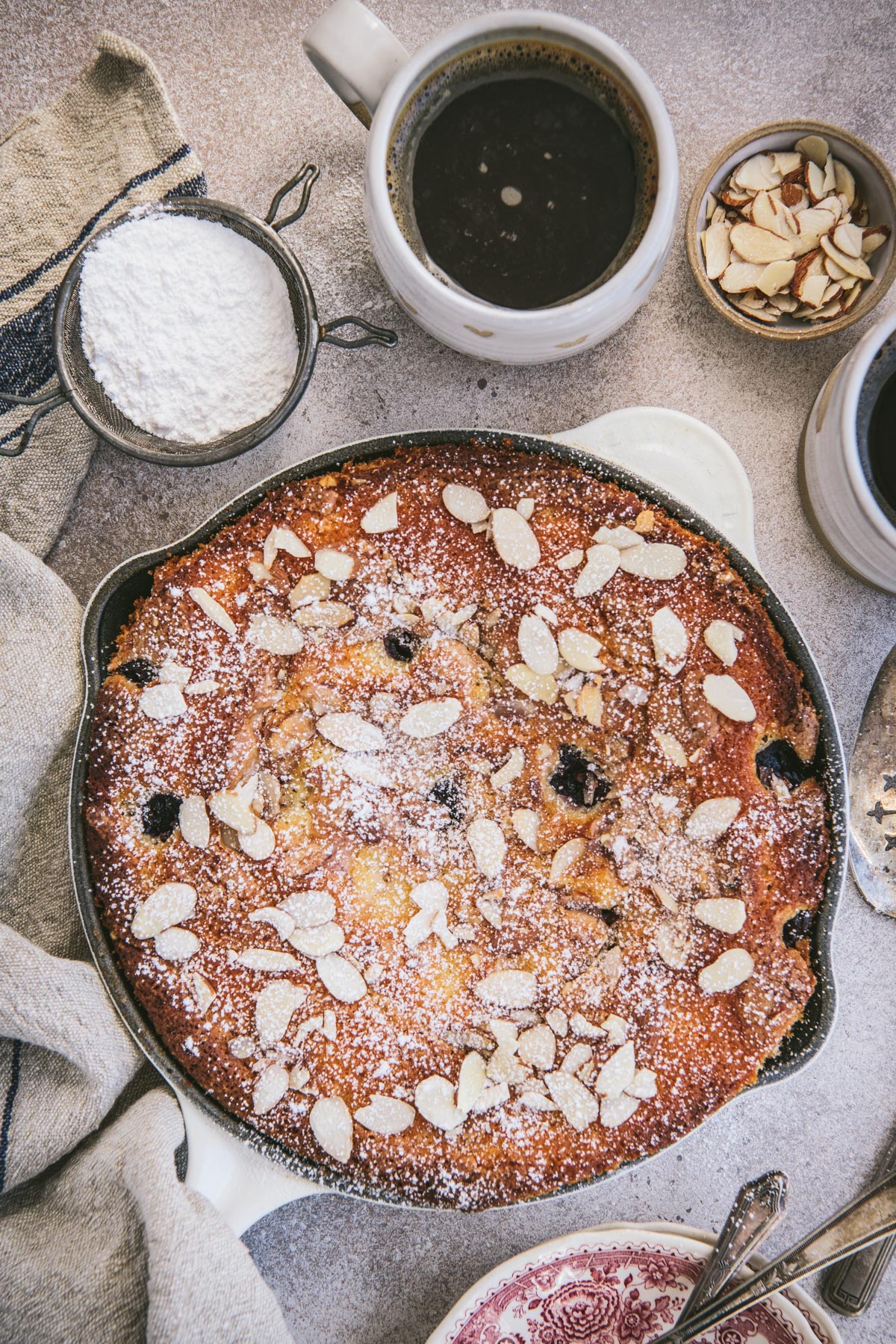 Overhead shot of a cherry skillet cake with almonds on a table.