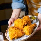 Hands serving a platter of oven fried cornflakes chicken