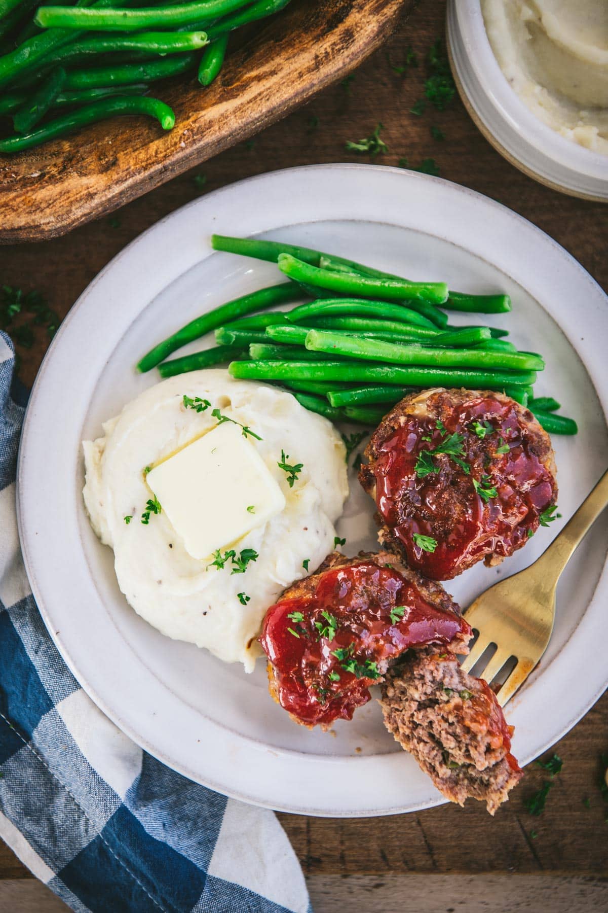 Overhead image of muffin tin meatloaf on a white plate with mashed potatoes and green beans.
