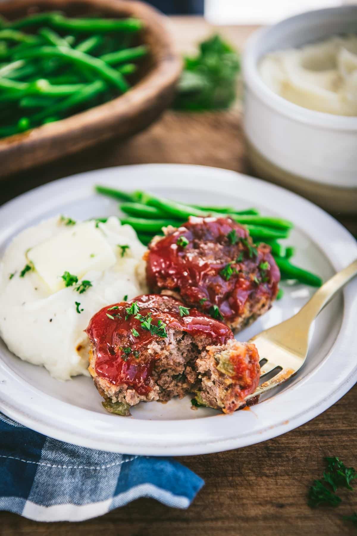 Bite of meatloaf on a gold fork on a white plate
