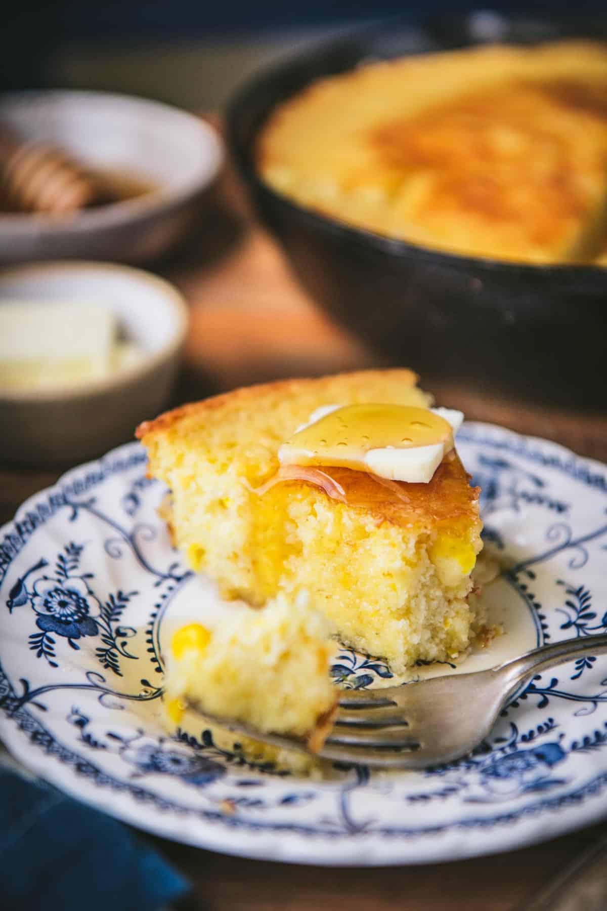 Close up side shot of butter and honey on top of a slice of cornbread with creamed corn and sour cream.