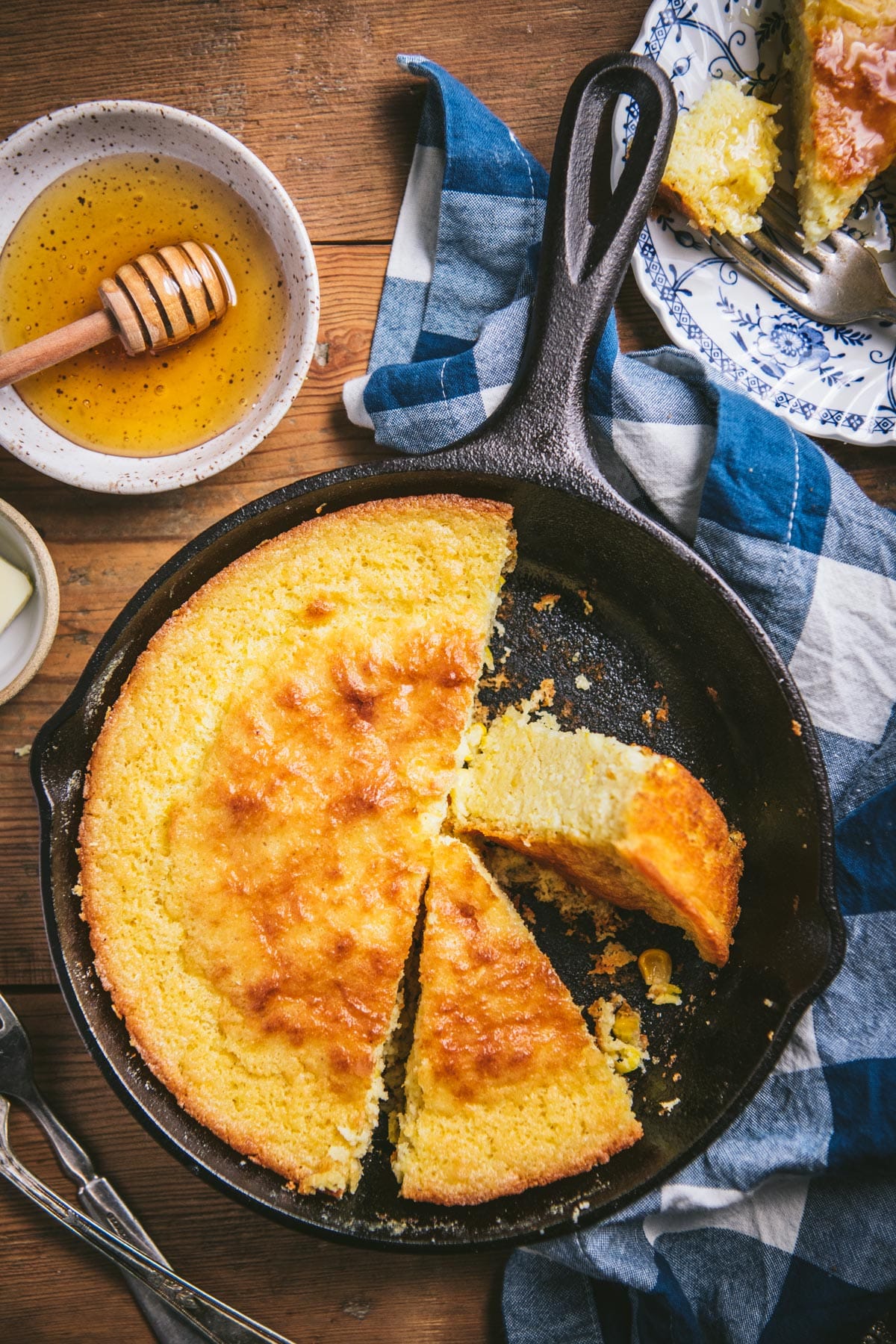 Overhead image of sour cream cornbread in a cast iron skillet on a wooden table.
