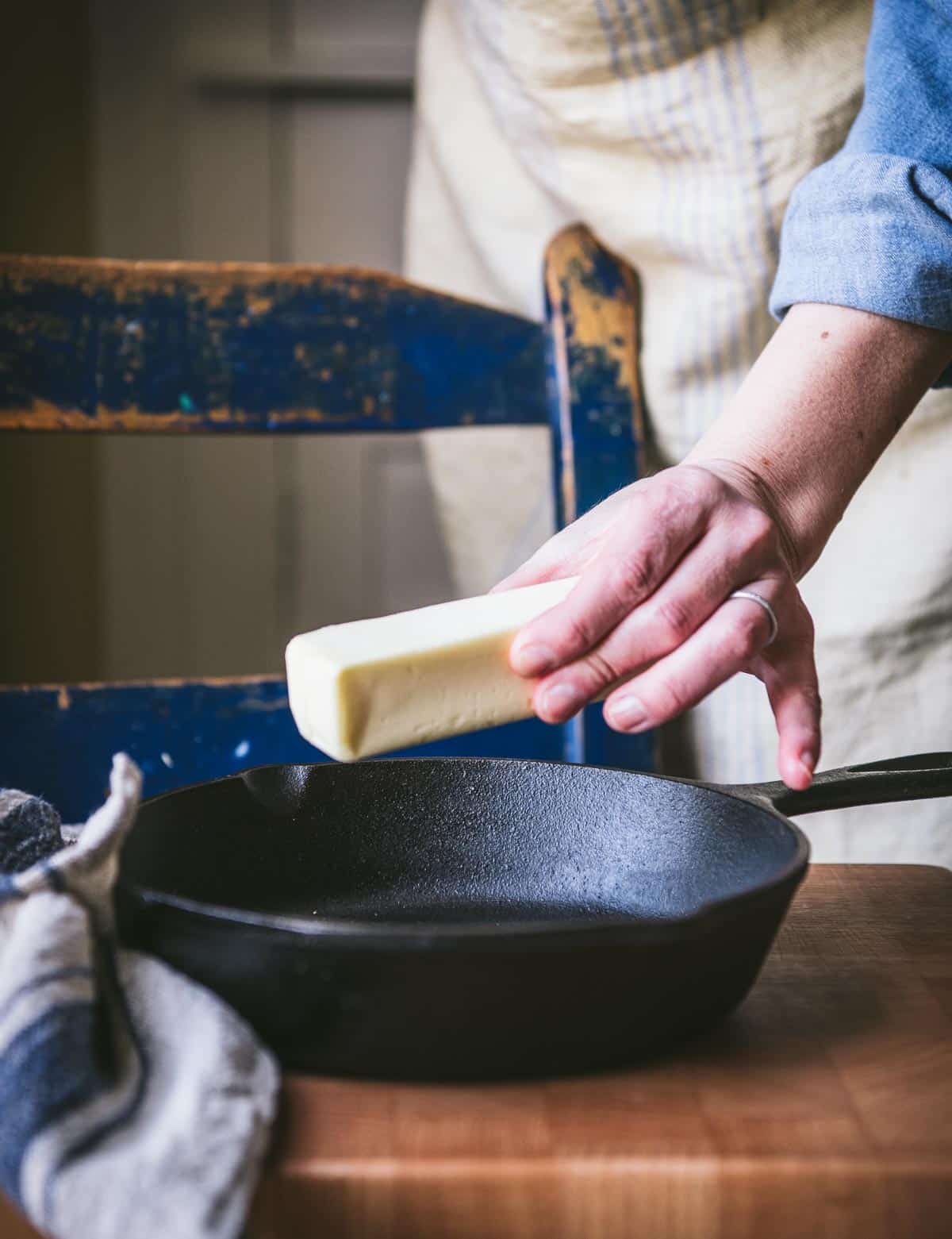 Placing a stick of butter in a cast iron skillet.