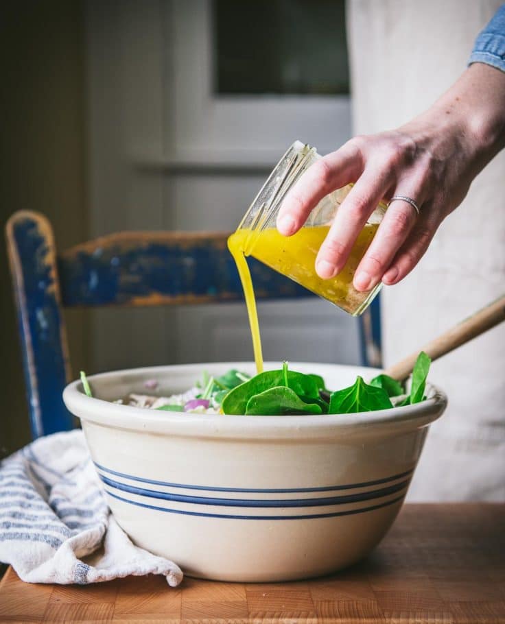 Pouring dressing over a bowl of tortellini salad.