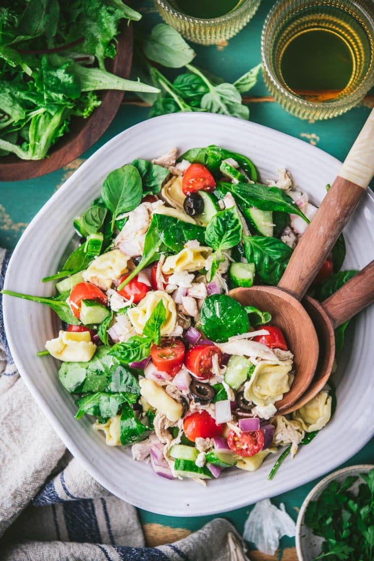 Overhead shot of a bowl of tortellini salad on a turquoise table with a side of biscuits and salad.