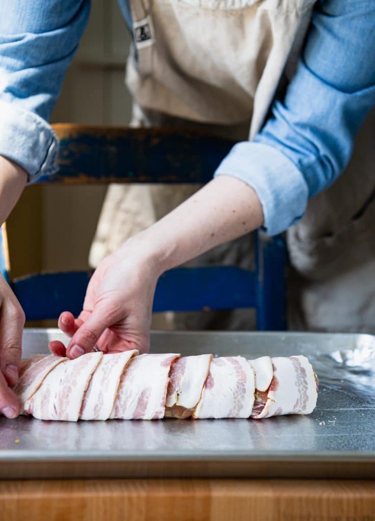 Process shot showing how to wrap pork tenderloin in bacon.