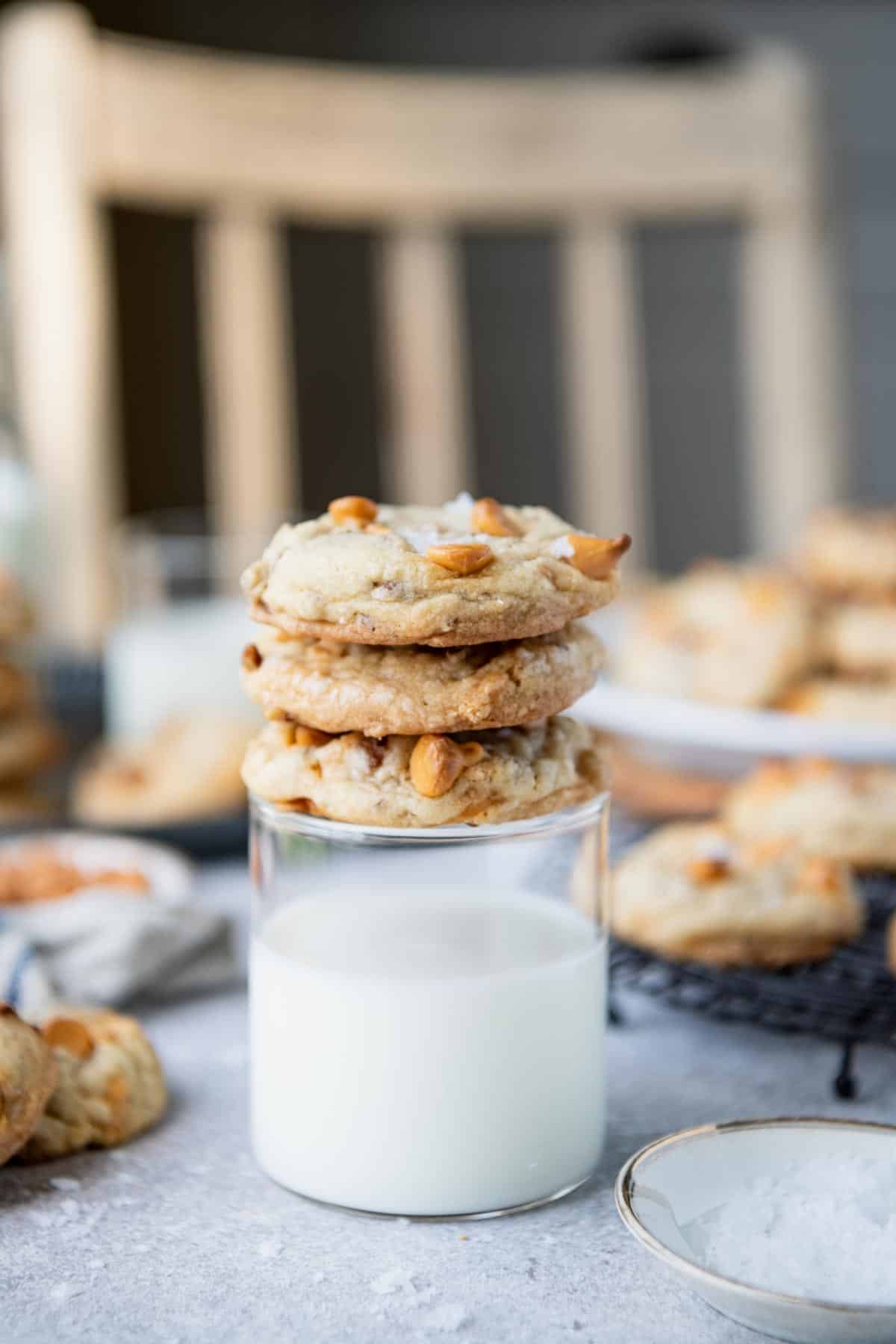 Three butterscotch cookies stacked on top of a glass of milk.