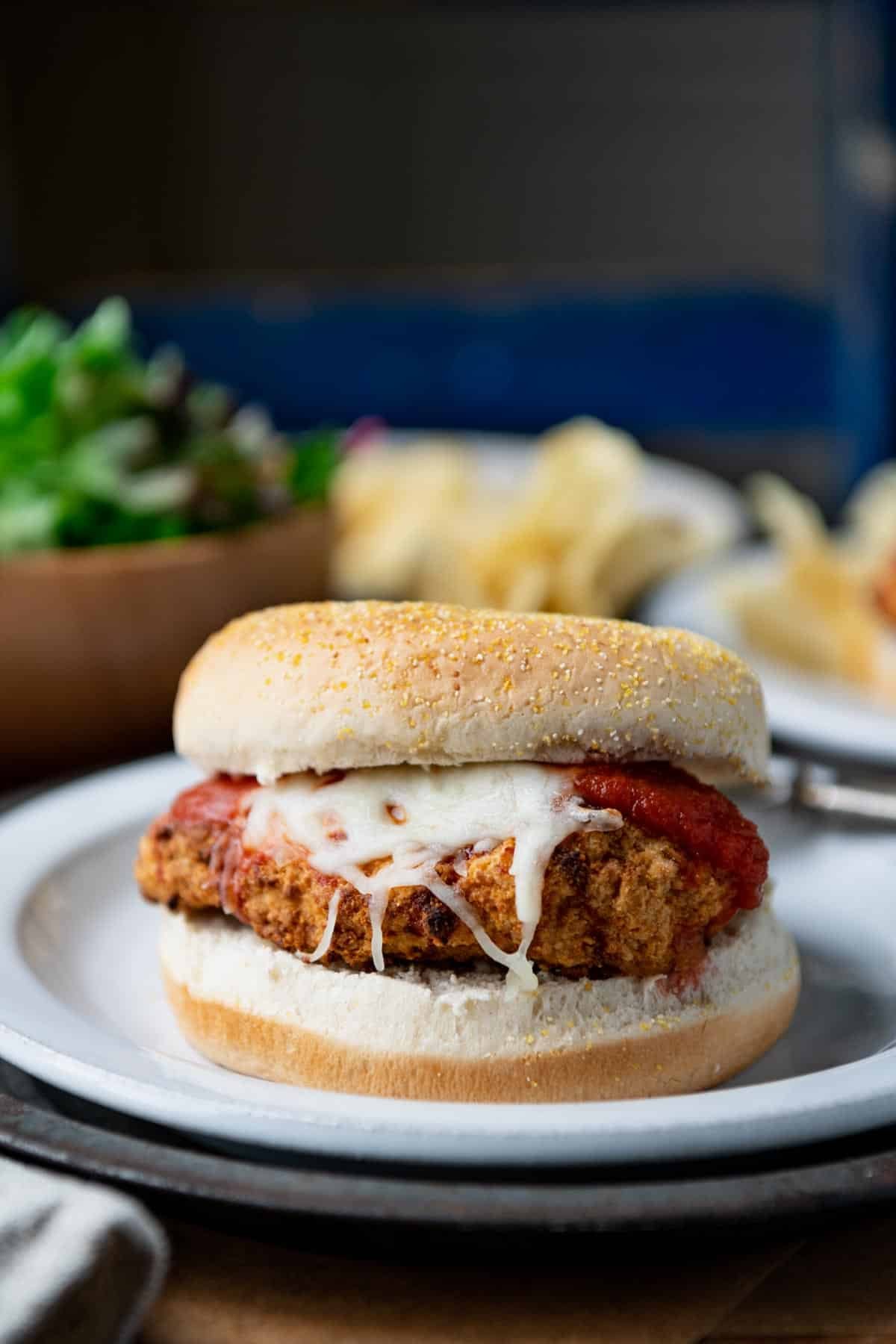 Close up front shot of a chicken parmesan sandwich with frozen chicken patties on a white dinner plate.