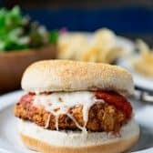 Close up front shot of an easy chicken parmesan sandwich recipe served on a white plate with a salad and chips.