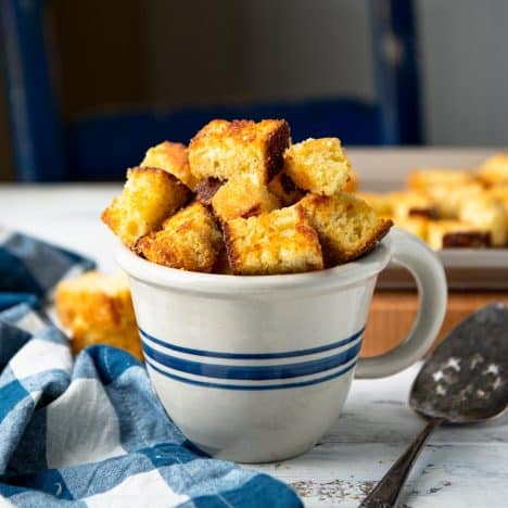 Square side shot of cornbread croutons in a mug on a table.
