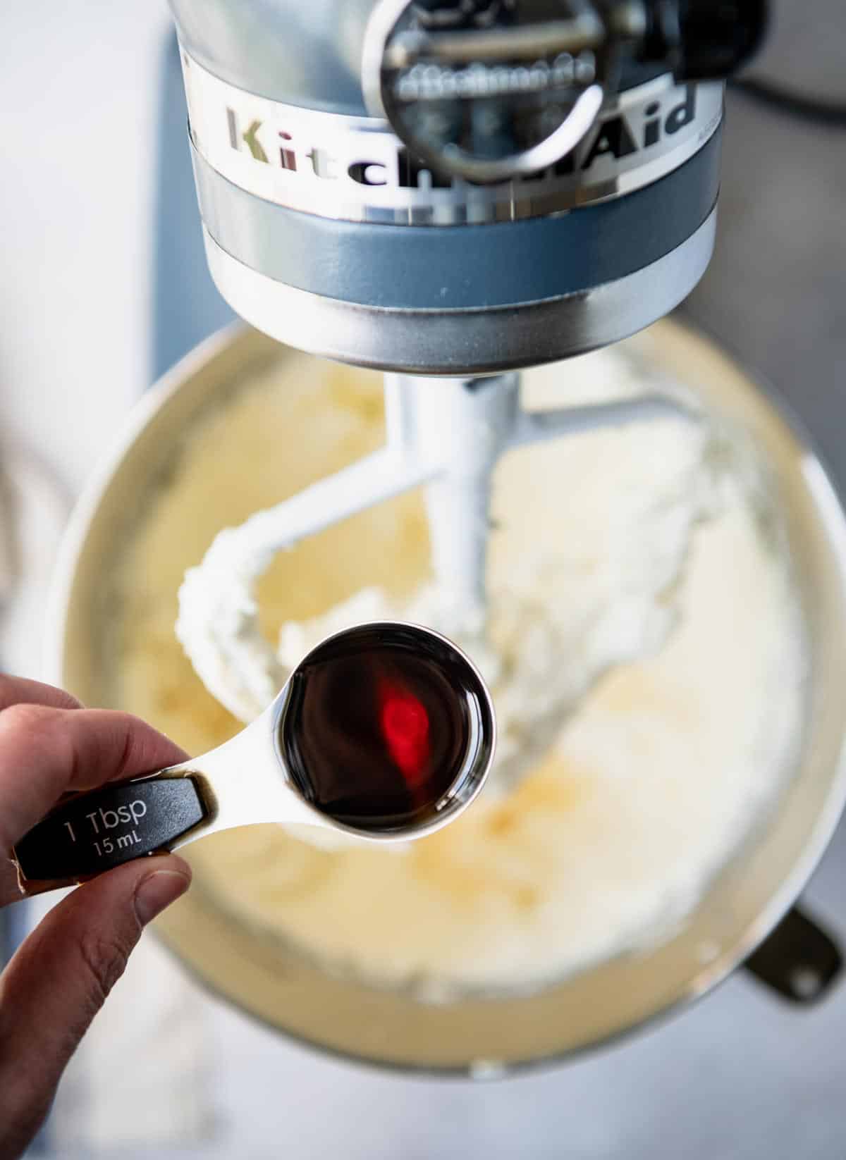 Adding vanilla extract to a bowl of cream cheese frosting.