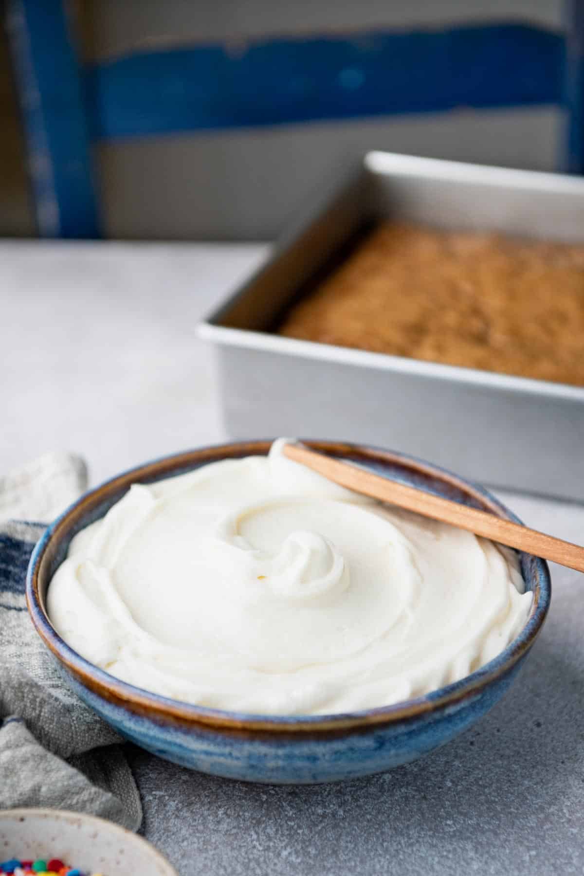 Side shot of easy cream cheese frosting in a bowl with a wooden spreader.