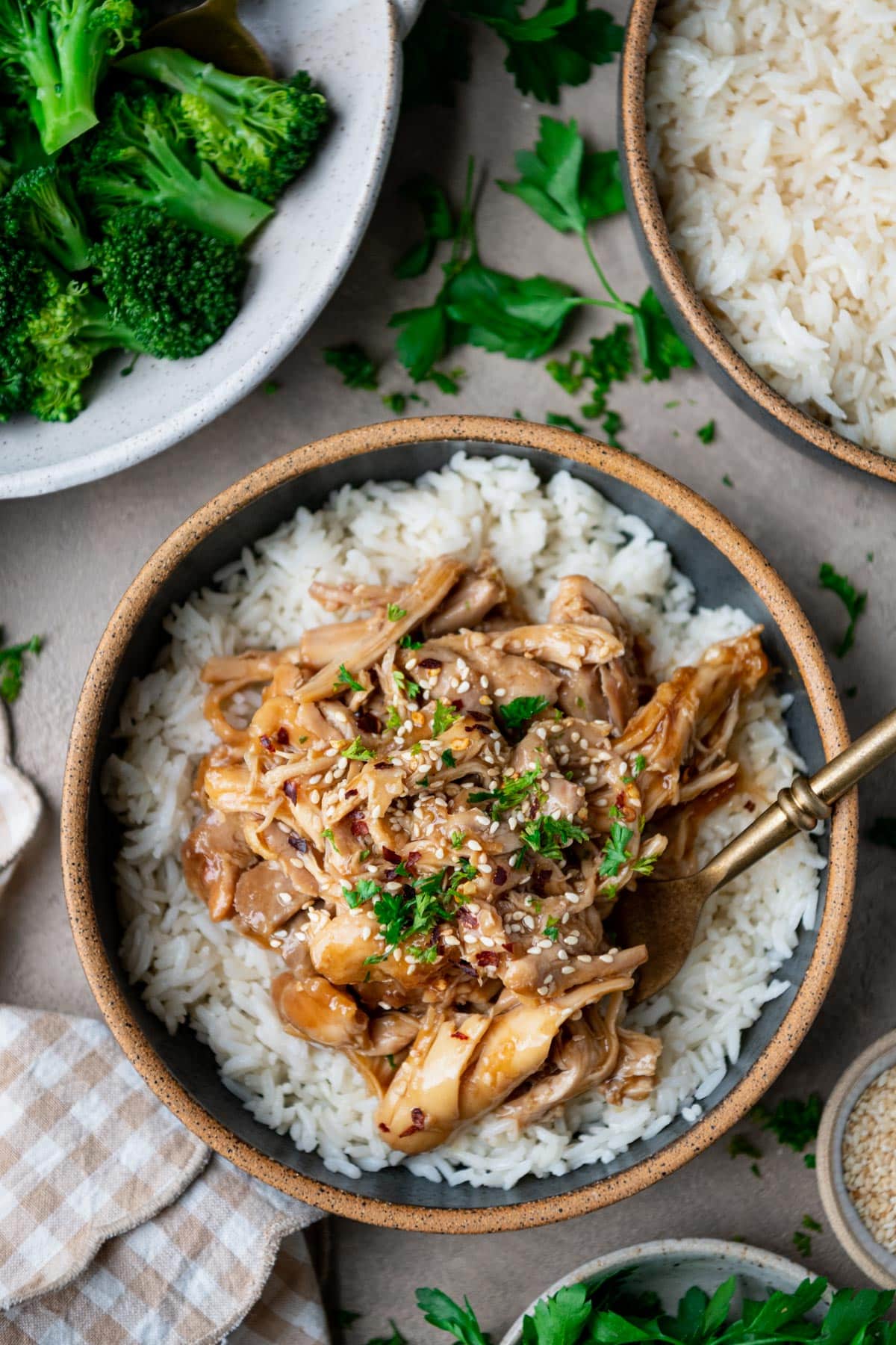 Fork in a bowl of crock pot shredded chicken with maple soy marinade over a bowl of rice.