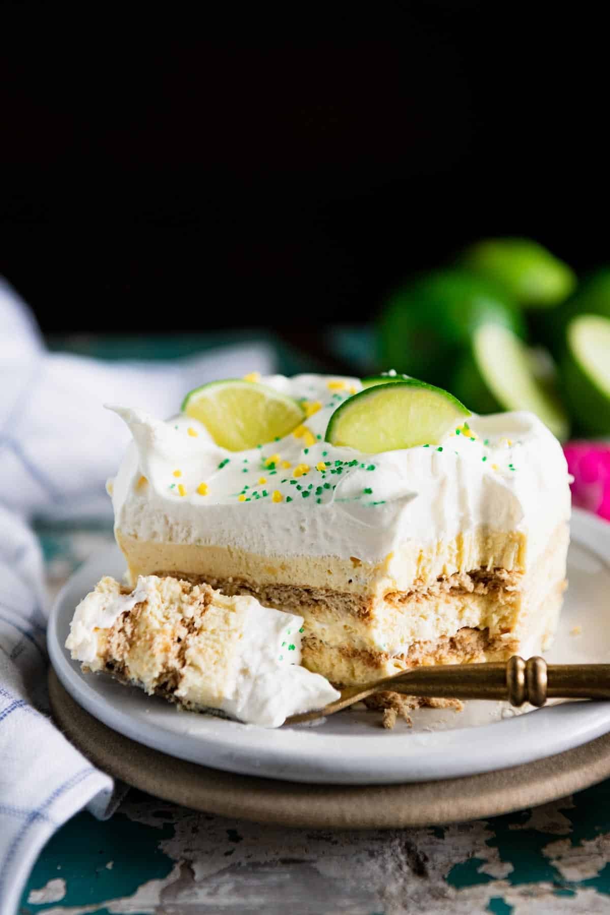 Close up side shot of key lime icebox cake on a table with a bite on a gold fork.