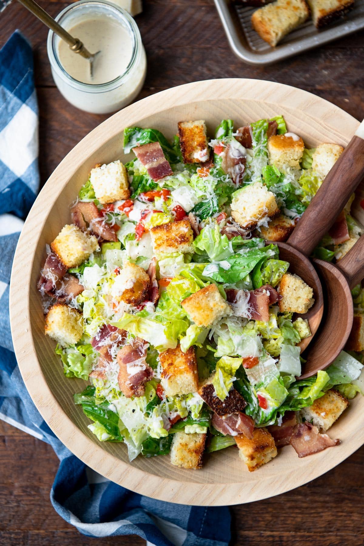 Close overhead shot of wooden servers in a bowl of caesar salad with cornbread croutons and bacon.