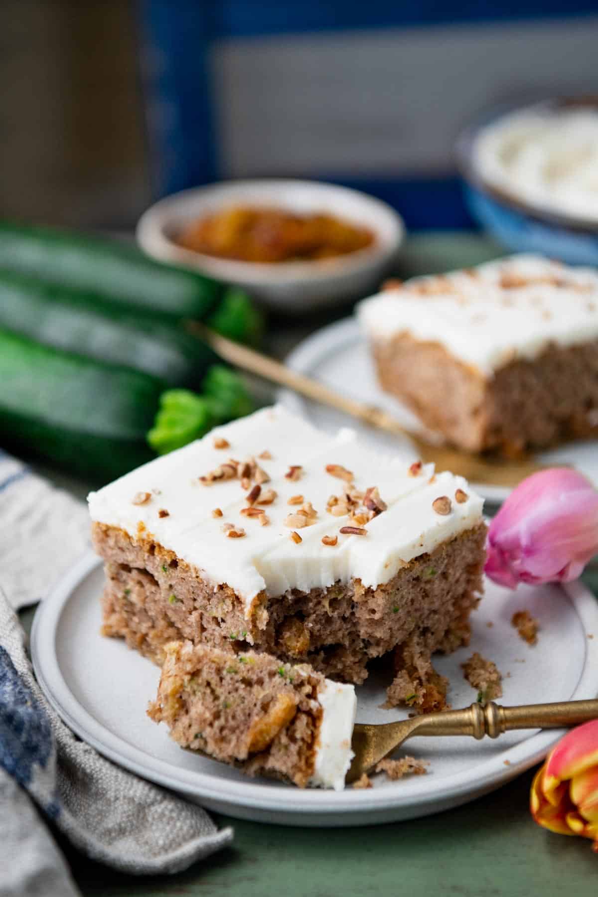 Side shot of a slice of the best zucchini cake recipe with cream cheese frosting on a table.