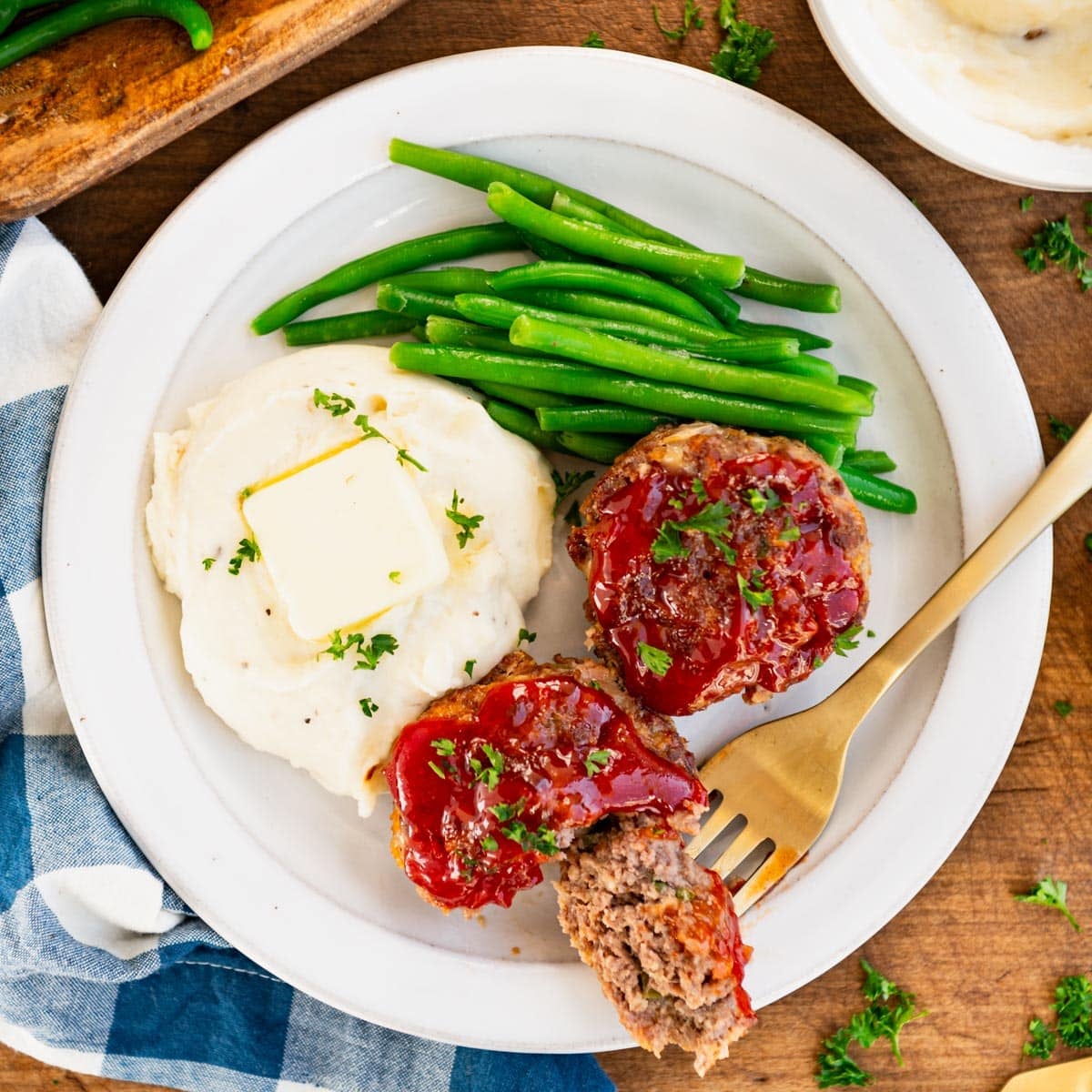 Square overhead shot of muffin tin meatloaf on a white plate with a bite on a fork.