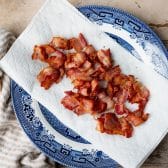 Crispy chopped bacon draining on paper towels on a plate.