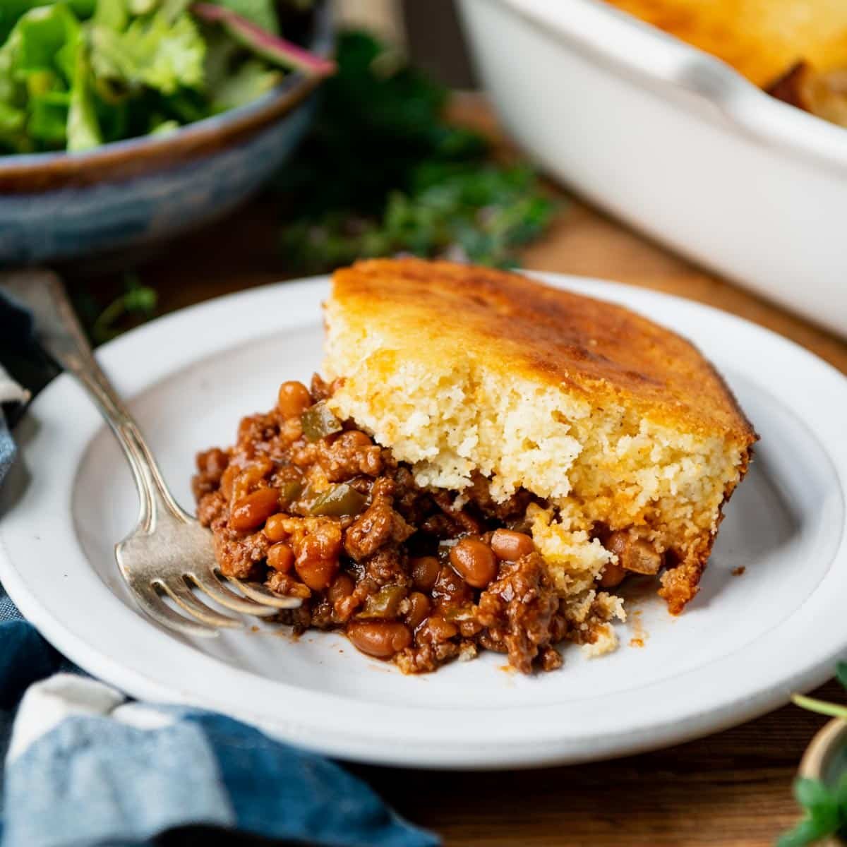 Square shot of a serving of cornbread casserole with ground beef on a white plate.