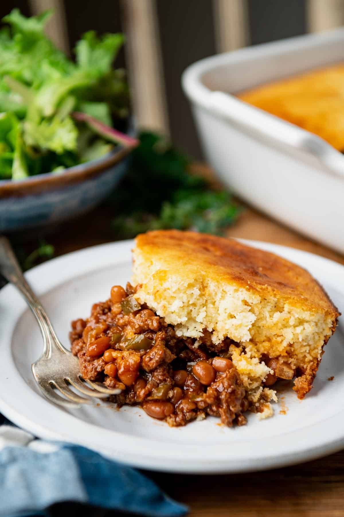 Front shot of a plate of ground beef and cornbread casserole on a table with a salad in the background.