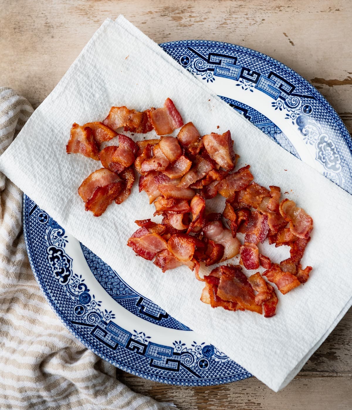 Crispy chopped bacon draining on paper towels on a plate.