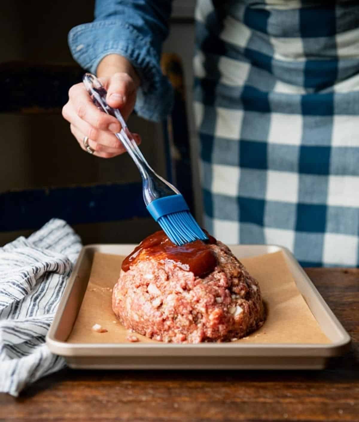 Brushing meatloaf with bbq sauce before baking.