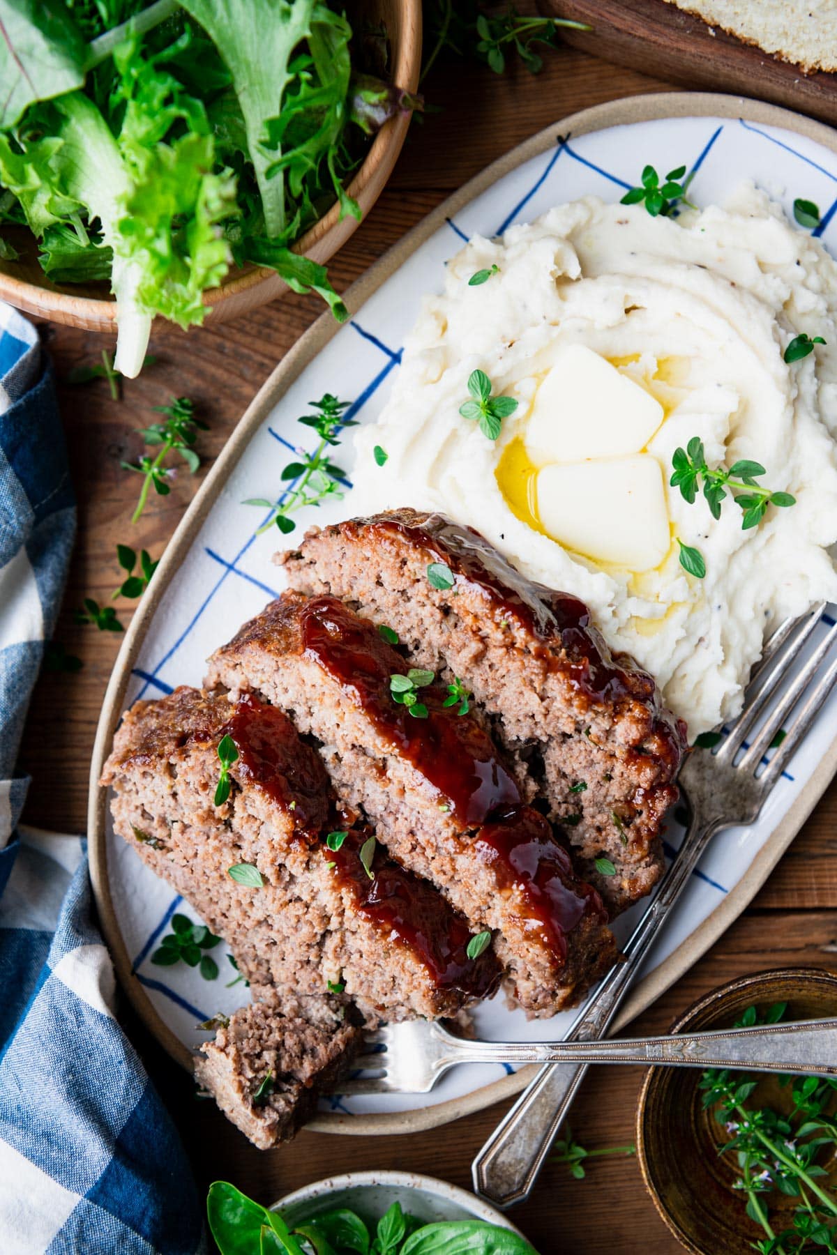Overhead image of barbecue meatloaf on a platter with mashed potatoes and a side salad.