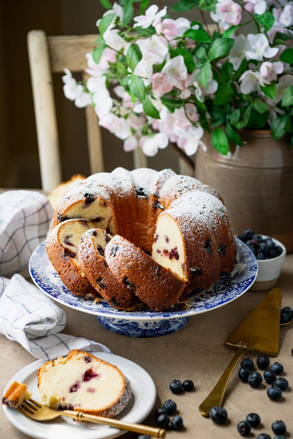 Side shot of blueberry pound cake on a table with flowers in the background.