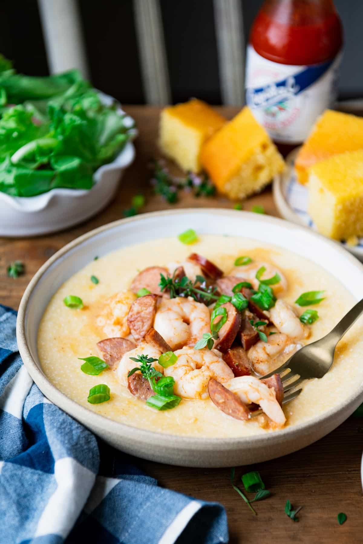 Side shot of a gold fork in a bowl of creamy New Orleans shrimp and grits with sausage.