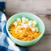 Cubed butter and grated cheddar cheese in a green bowl.