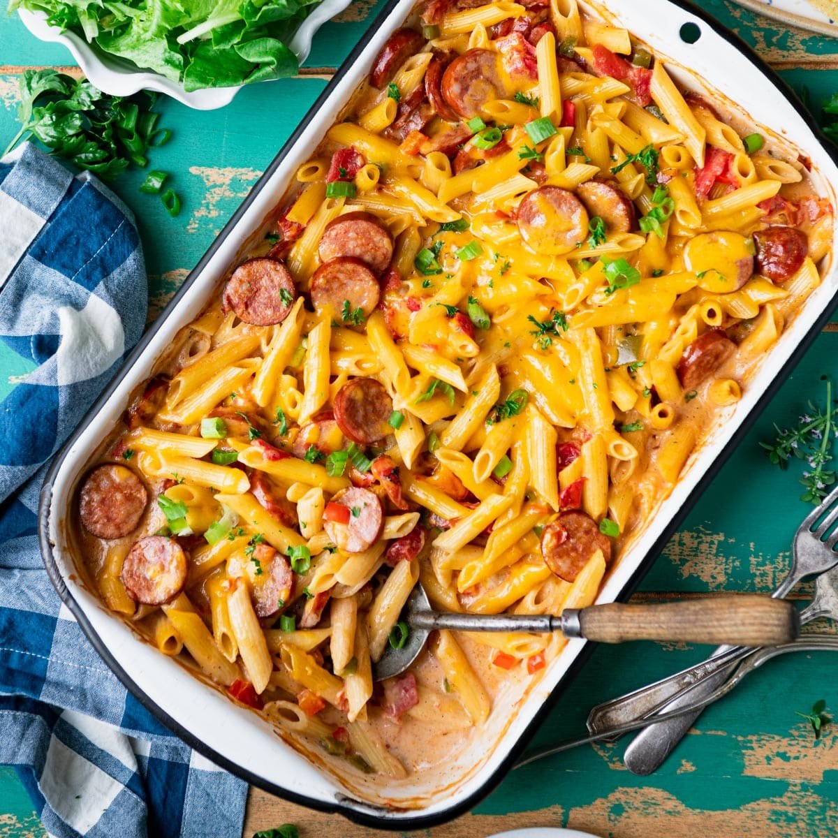 Square overhead image of a cajun sausage pasta casserole on a turquoise table.