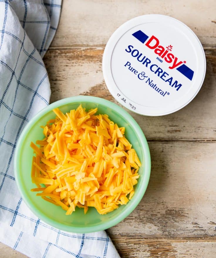Sour cream and a bowl of grated cheddar cheese.