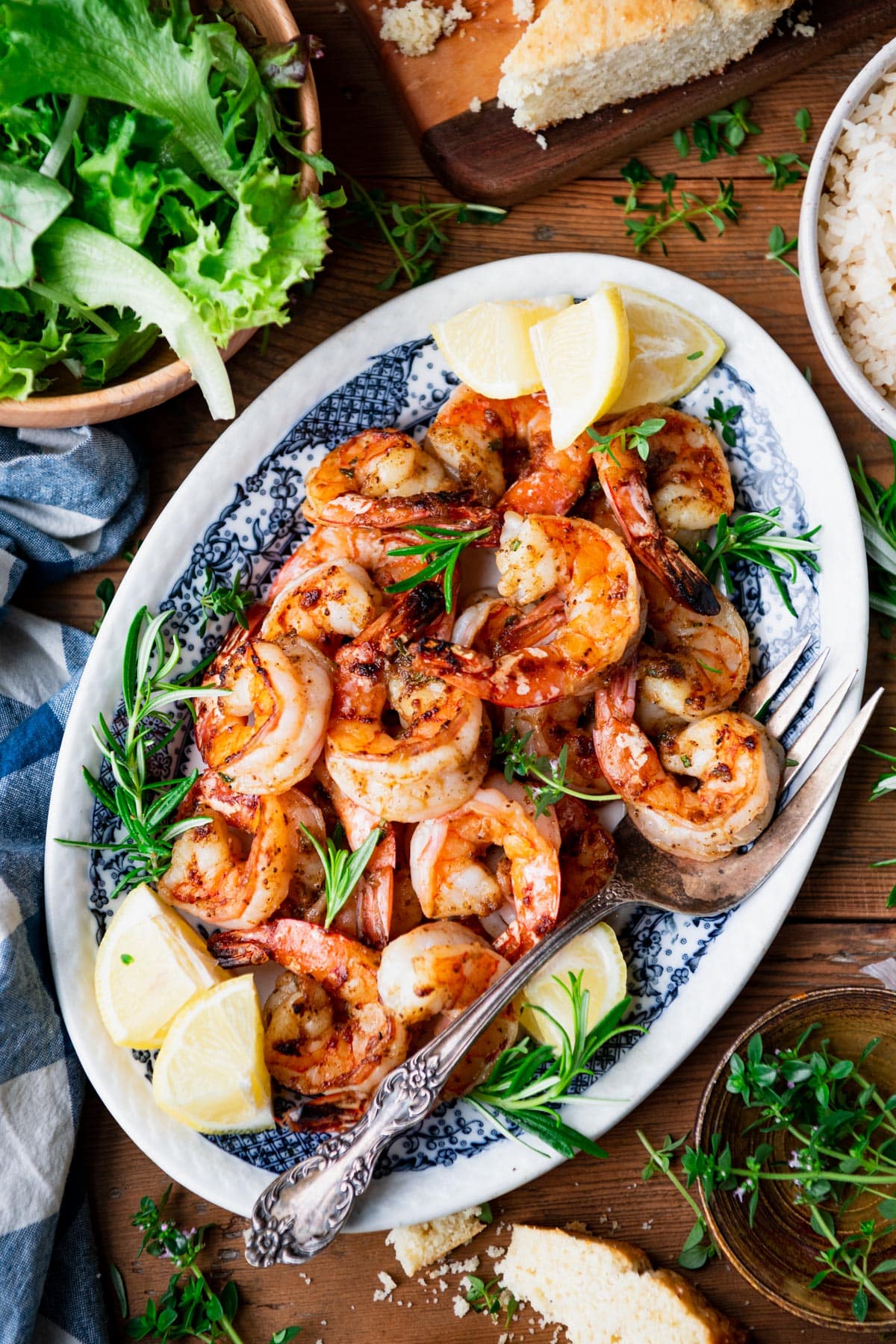 Overhead shot of a platter of broiled shrimp with fresh lemon wedges and rosemary.