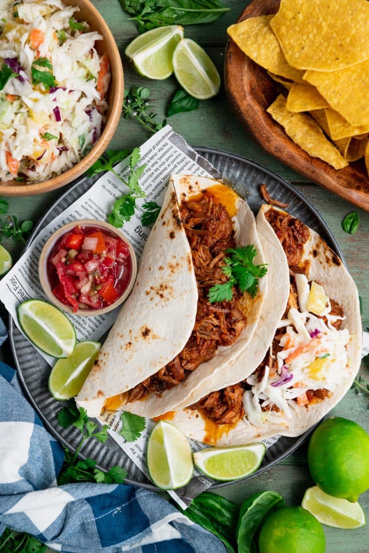 Overhead shot of a tin plate with two slow cooker pulled pork tacos and a side of pineapple slaw.