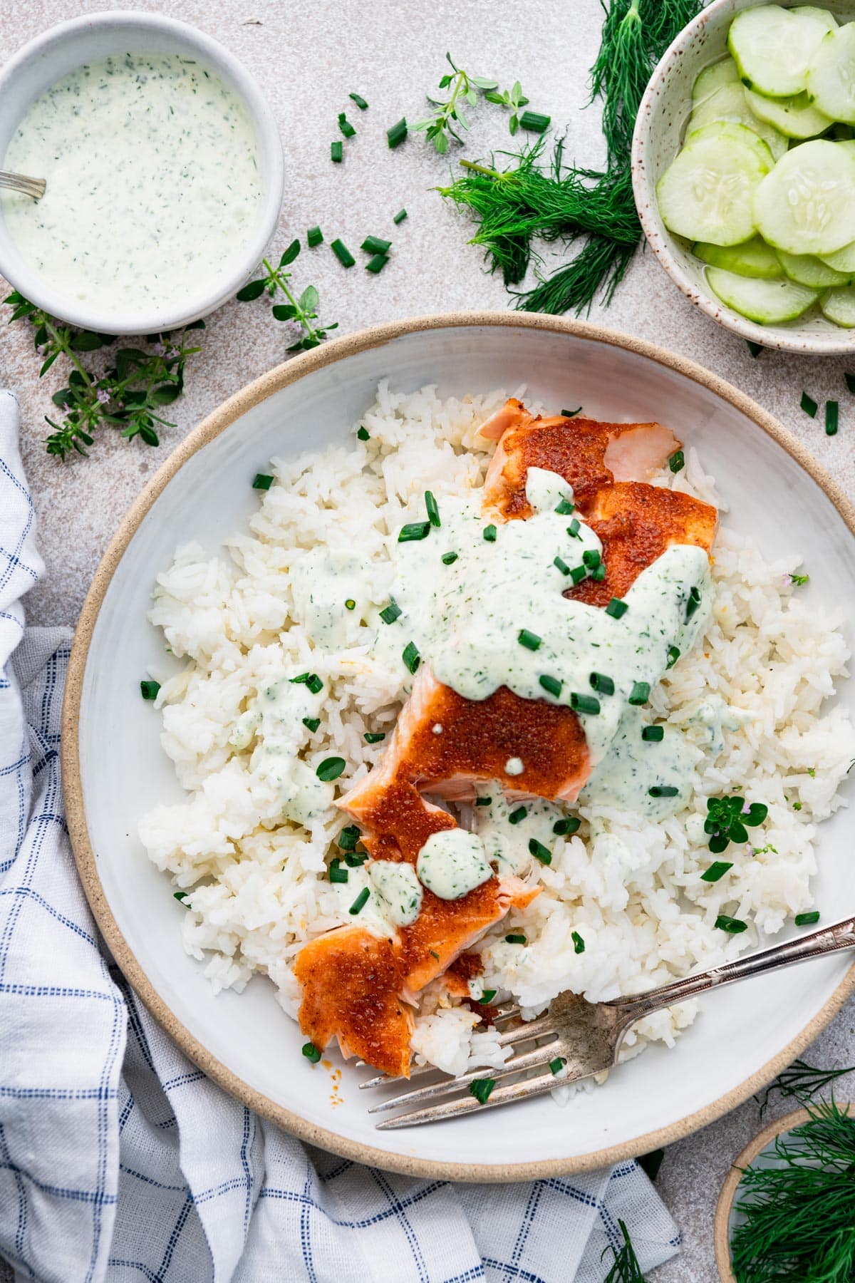Close overhead image of roasted old bay salmon with a side of rice and marinated cucumbers.