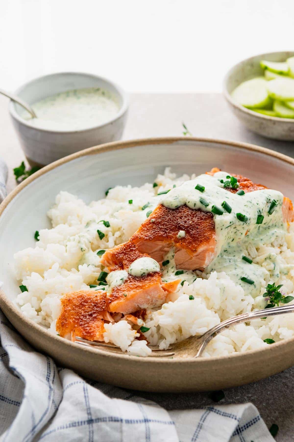 Side shot of a bowl of old bay salmon with rice and a creamy dill sauce.