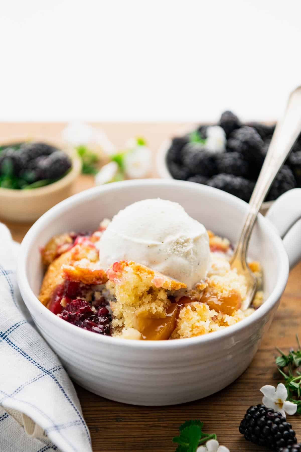 Side shot of blackberry cobbler with peaches in a bowl with ice cream on top.