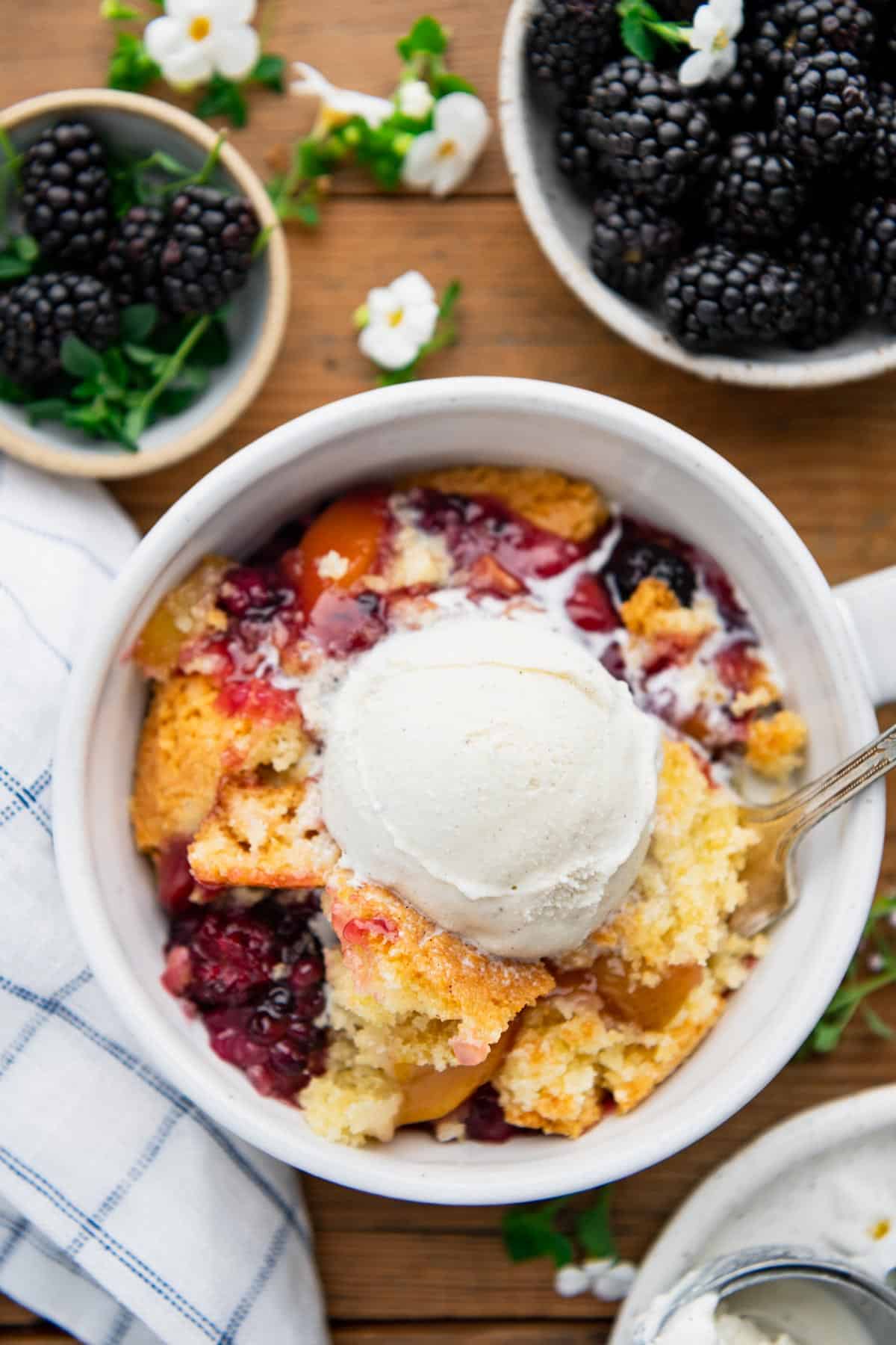 Overhead image of a white bowl full of southern blackberry and peach cobbler with a scoop of vanilla ice cream on top.