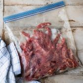 Sliced flank steak marinating in a large Ziploc bag.