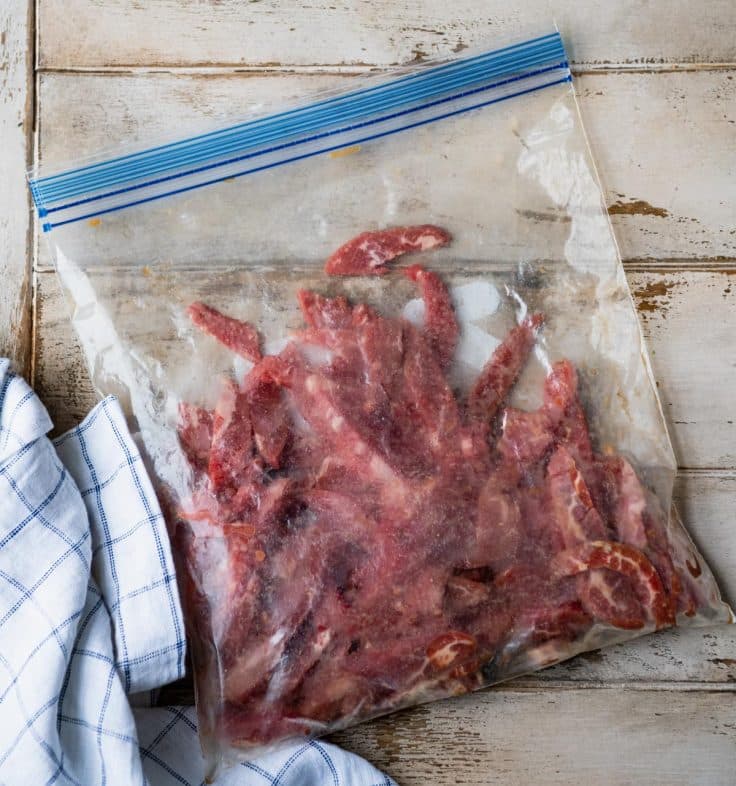 Sliced flank steak marinating in a large Ziploc bag.