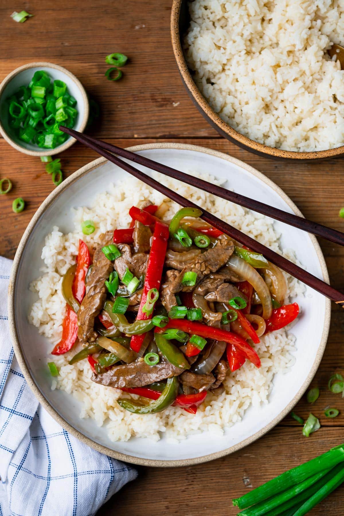 Overhead image of the best pepper steak recipe served with rice on a wooden table and garnished with green onion.