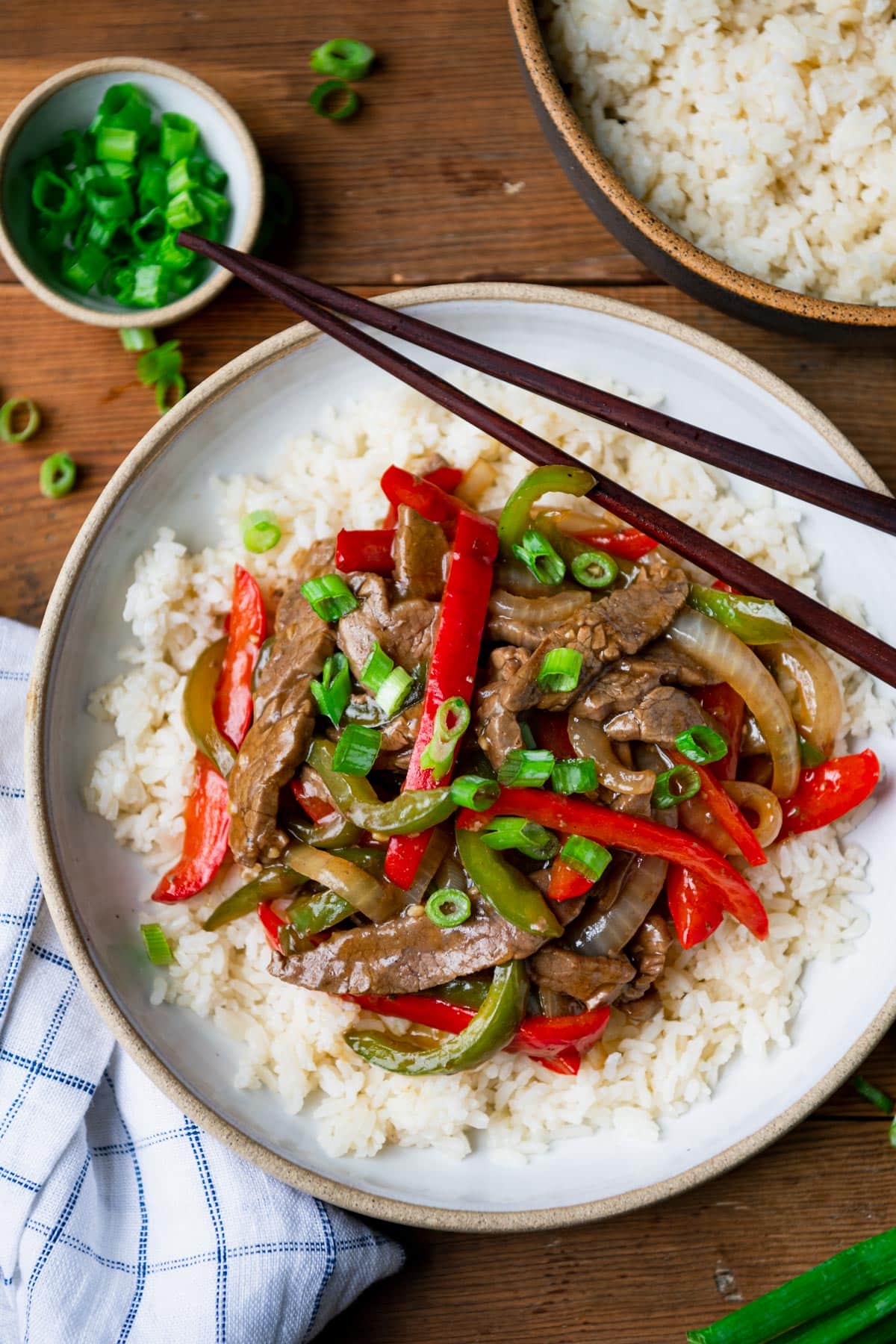 Close overhead shot of Chinese pepper steak with onion on a bed of white rice with chopsticks.