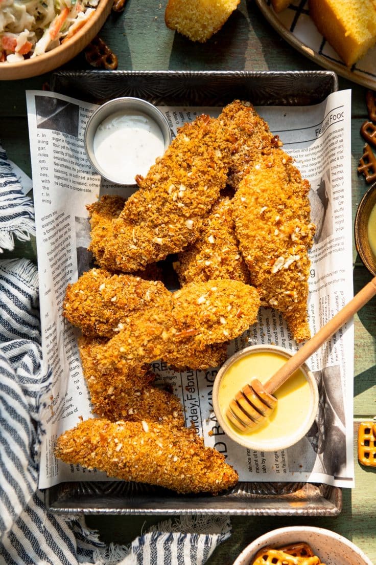 Baked pretzel crusted chicken in a tray with honey mustard sauce and ranch for dipping.