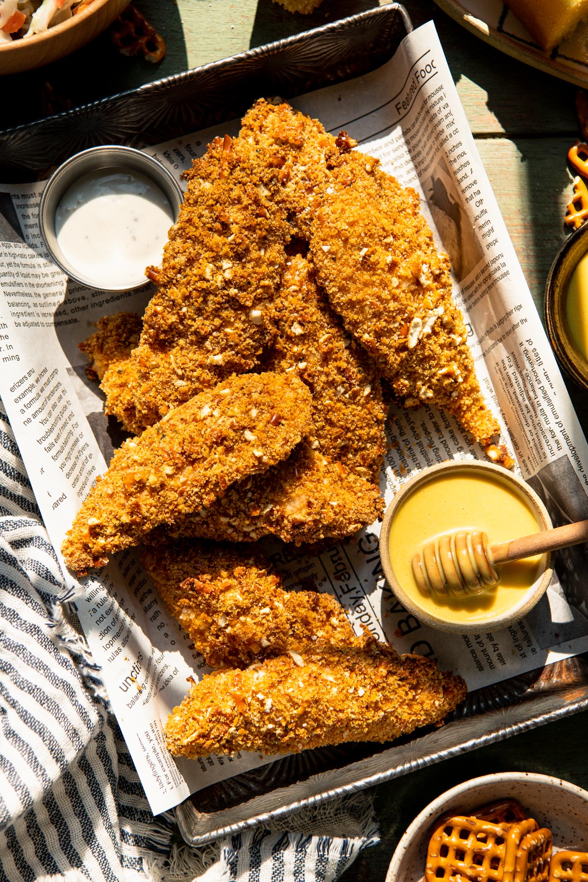 Close overhead image of pretzel crusted chicken strips served with ranch and honey mustard dip.